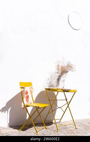 sedia in metallo combinata con tavolo giallo su parete bianca per un tocco minimalista Foto Stock
