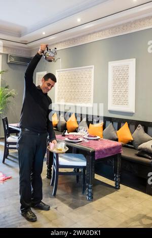 Il server del ristorante mostra un modo tradizionale per versare il tè alla menta a Marrakech, Marocco Foto Stock