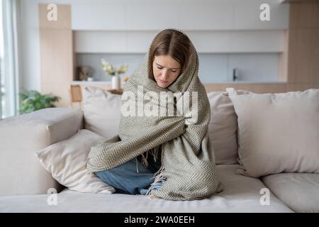 Donna depressa e depressa che piange seduta con gli occhi chiusi avvolta a quadri. Influenza, stagione covid Foto Stock