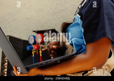 Un tecnico professionista che cerca online una nuova ventola per la sostituzione della vecchia dopo aver individuato un componente interno del sistema hvac esterno guasto durante il controllo eseguito dal cliente Foto Stock