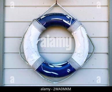 Un anello di salvataggio blu e bianco, salvagente o salvagente appeso a un muro vicino alla spiaggia in estate Foto Stock