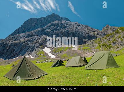 Tende di cacciatori di montagna su un prato verde di fronte a un imponente sfondo di montagna sotto un cielo azzurro, Alpspitze, Kreuzeck, Osterfelder Abfahrt Foto Stock