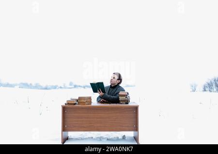 Un giovane e bello uomo intelligente con una giacca siede a un tavolo in un campo e legge libri antichi in inverno Foto Stock