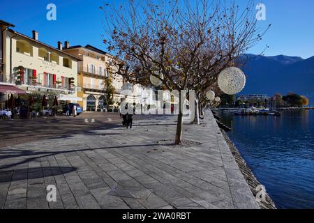 Platano con decorazioni natalizie e case color pastello sul lungolago Piazza Giuseppe Motta del Lago maggiore ad Ascon Foto Stock