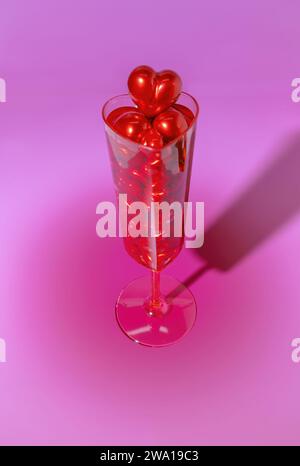 Un bicchiere di champagne a forma di cuore pieno di cuori rossi per San Valentino Foto Stock