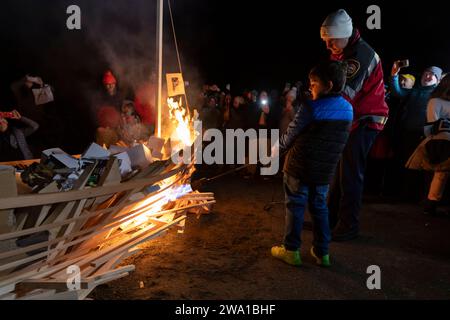 Des Moines, Washington, USA. 31 dicembre 2023. Un ufficiale con le torce South King Fire and Rescue lancia una barca cerimoniale con un giovane assistente al Burning Boat Festival al Des Moines Beach Park. Le persone sono state invitate a scrivere appunti di obiettivi personali per il nuovo anno o dolori che devono essere purgati dall'universo che sarà collocato nella barca. Credito: Paul Christian Gordon/Alamy Live News Foto Stock