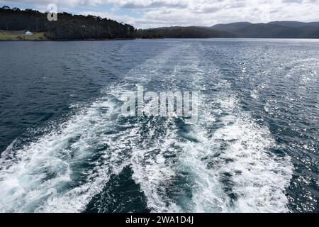 Stern onde da una barca che naviga attraverso Carnavon Bay con la Master Shipwright's House nella Colonia penale di Port Arthur in Tasmania, Australia Foto Stock