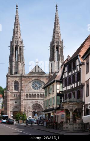 Chiesa con due torri dei Santi Pietro e Paolo e sulla destra il pozzo d'acqua a sei secchi in stile rinascimentale nel centro della città di Obernai, Francia Foto Stock