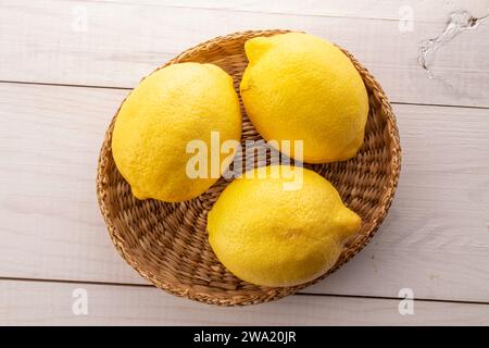 Tre limoni organici di colore giallo brillante con piastra di paglia su tavolo in legno, macro, vista dall'alto. Foto Stock