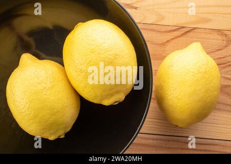 Tre limoni maturi gialli su un piatto in ceramica nera su un tavolo in legno, vista ravvicinata dall'alto. Foto Stock