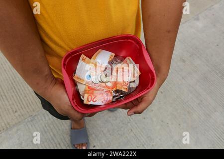 Tiaong, Filippine. 1 gennaio 2024: Nelle province rurali, le famiglie povere filippine costruiscono strade a pedaggio amichevoli con una corda e un cartello di felice anno nuovo. Auto, tricicli o pedoni sono incoraggiati a fare donazioni "grazie", generalmente solo pochi pesos, senza impegno, sempre con sorriso e talvolta abbelliti da pochi passi di danza. Una tradizione che era praticata solo in alcune regioni e che si è diffusa in quasi tutto il paese dai giorni duri dell'epidemia di COVID 19. Ad esempio, oltre 1 km, in alcuni luoghi è possibile contare fino a quindici fermate. Crediti: Kevin Izorce/Alamy Live News Foto Stock