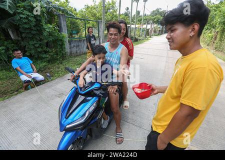 Tiaong, Filippine. 1 gennaio 2024: Nelle province rurali, le famiglie povere filippine costruiscono strade a pedaggio amichevoli con una corda e un cartello di felice anno nuovo. Auto, tricicli o pedoni sono incoraggiati a fare donazioni "grazie", generalmente solo pochi pesos, senza impegno, sempre con sorriso e talvolta abbelliti da pochi passi di danza. Una tradizione che era praticata solo in alcune regioni e che si è diffusa in quasi tutto il paese dai giorni duri dell'epidemia di COVID 19. Ad esempio, oltre 1 km, in alcuni luoghi è possibile contare fino a quindici fermate. Crediti: Kevin Izorce/Alamy Live News Foto Stock