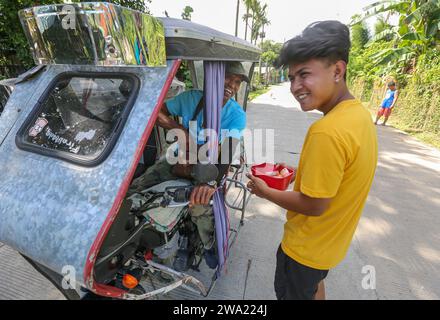 Tiaong, Filippine. 1 gennaio 2024: Nelle province rurali, le famiglie povere filippine costruiscono strade a pedaggio amichevoli con una corda e un cartello di felice anno nuovo. Auto, tricicli o pedoni sono incoraggiati a fare donazioni "grazie", generalmente solo pochi pesos, senza impegno, sempre con sorriso e talvolta abbelliti da pochi passi di danza. Una tradizione che era praticata solo in alcune regioni e che si è diffusa in quasi tutto il paese dai giorni duri dell'epidemia di COVID 19. Ad esempio, oltre 1 km, in alcuni luoghi è possibile contare fino a quindici fermate. Crediti: Kevin Izorce/Alamy Live News Foto Stock