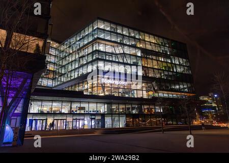 Vista serale sulla sede centrale del Booking.com ad Amsterdam, Paesi Bassi, con finestre illuminate nella facciata di vetro Foto Stock