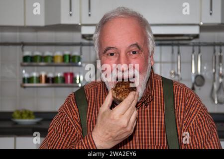 Un uomo anziano ama la polpetta fatta in casa dalla moglie in cucina come se fosse il regalo più prezioso. Foto Stock