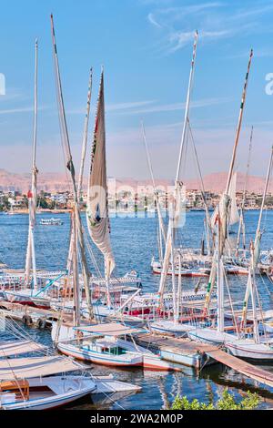 Luxor, Egitto - dicembre 26 2023: Tradizionali traghetti a motore e barche a vela in feluca ormeggiate lungo il Nilo Foto Stock