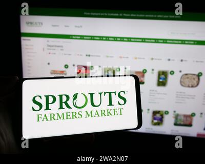 Persona che possiede un telefono cellulare con il logo della società di vendita al dettaglio americana sprouts Farmers Market Inc. Davanti alla pagina Web. Concentrarsi sul display del telefono. Foto Stock