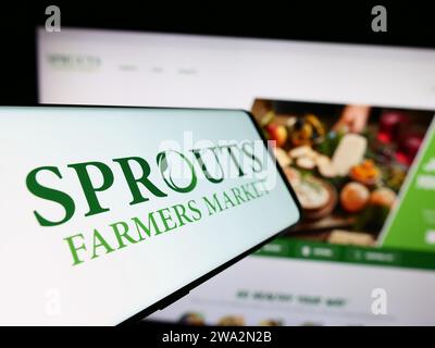 Telefono cellulare con logo della società di vendita al dettaglio americana Sceuts Farmers Market Inc. Davanti al sito Web. Mettere a fuoco il display centrale sinistro del telefono. Foto Stock