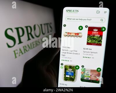Persona che possiede il cellulare con la pagina Web della società di vendita al dettaglio statunitense sprouts Farmers Market Inc. Davanti al logo. Concentrarsi sul centro del display del telefono. Foto Stock