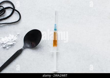 Vista dall'alto di una siringa, cucchiaio nero, polvere e corda, strumenti per l'uso di cocaina ed eroina su un tavolo bianco, foto concettuale dell'uso di droghe Foto Stock