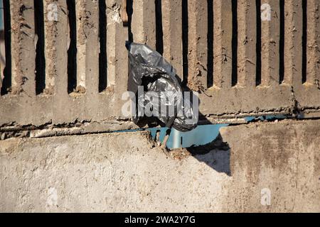 Un sacchetto di plastica vuoto nero pesa su una recinzione di cemento in una città al sole durante il giorno in Ucraina, spazzatura, inquinamento ambientale Foto Stock