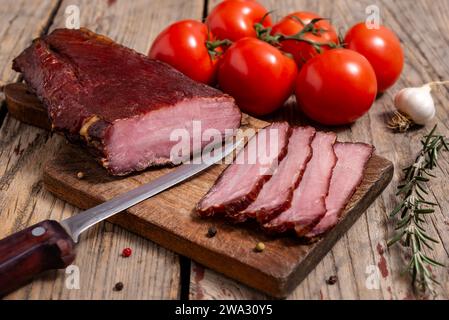 Tagliere con carne secca, verdure, spezie e coltello da cucina su un tavolo di legno. Messa a fuoco selettiva. Foto Stock