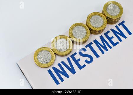 Monete britanniche da una sterlina in colonne di dimensioni crescenti accanto a un documento di investimento. Niente persone. Foto Stock