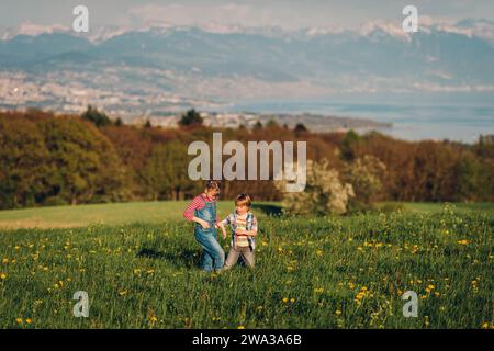 Due bambini, fratellino e sorella maggiore, che giocano insieme nei campi svizzeri con vista sul lago di Ginevra e sulle montagne francesi dell'alta Savoia. Immagine t Foto Stock