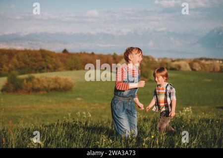 Due bambini, fratellino e sorella maggiore, che giocano insieme nei campi svizzeri con vista sul lago di Ginevra e sulle montagne francesi dell'alta Savoia. Immagine t Foto Stock