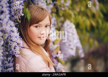 Ritratto primaverile di adorabile bambina di 9-10 anni che posa in fiori di glicine Foto Stock