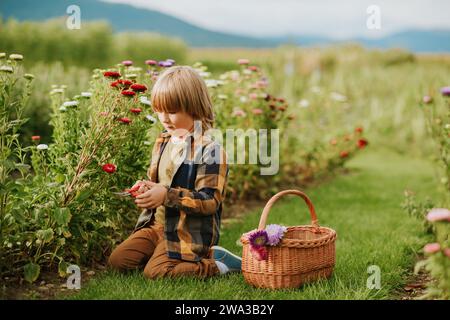 Simpatico bambino che lavora nel giardino autunnale, bambino che si prende cura del crisantemo colorato, giardiniere che si gode una giornata calda e soleggiata all'aperto Foto Stock