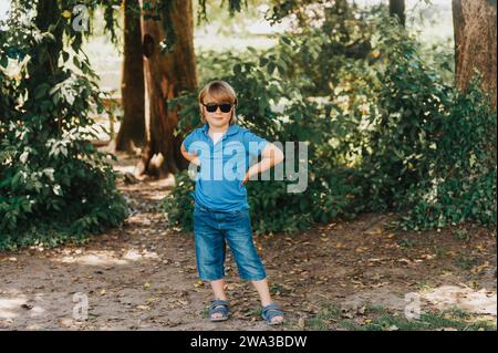 Ritratto all'aperto di un adorabile bambino che indossa una polo blu e occhiali da sole alla moda Foto Stock