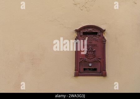 Antica cassetta postale del Regio servizio postale italiano (Regie Poste italiane) in ghisa rossa su un muro dipinto di giallo, Toscana, Italia Foto Stock