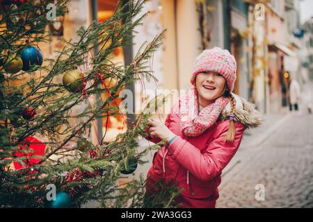 Bambina felice che gioca con l'albero di Natale per le strade della vecchia città europea, viaggi per le vacanze con i bambini, immagine scattata a Losanna, Svizzera Foto Stock