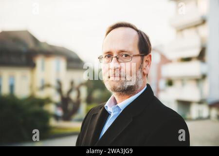 Ritratto all'aperto di un uomo di 50 anni che indossa un cappotto nero e occhiali da vista Foto Stock
