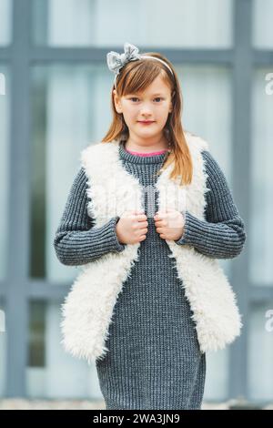 Ritratto all'aperto di una graziosa ragazza di 8-9 anni che indossa un pullover grigio e un gilet bianco in pelliccia sintetica Foto Stock