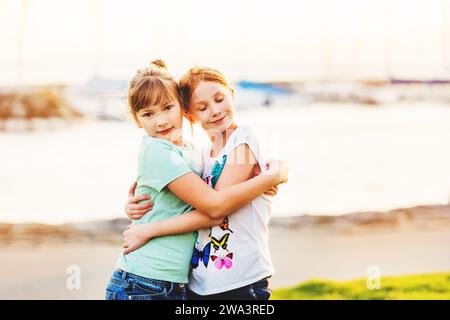 Due ragazze di 9-10 anni che giocano insieme fuori, abbracciandosi, ora d'oro Foto Stock