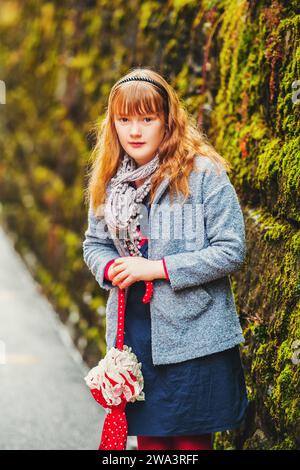 Ritratto all'aperto di una graziosa bambina di 9-10 anni, che indossa un cappotto e una sciarpa grigi, che regge un ombrello Foto Stock