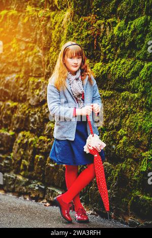 Ritratto all'aperto di una graziosa bambina di 9-10 anni, che indossa un cappotto e una sciarpa grigi, che regge un ombrello Foto Stock