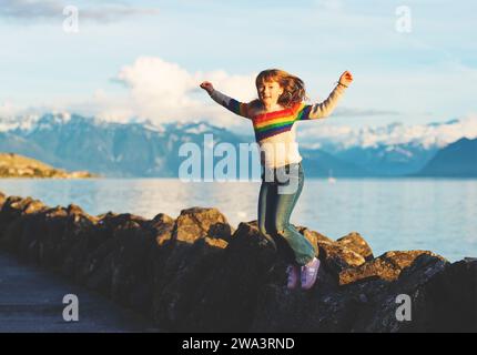 Bambina felice e giovane che gioca vicino al lago di ginevra al tramonto, braccia spalancate Foto Stock