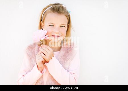 Ritratto romantico di adorabile bambina con capelli biondi e occhi blu, con abiti rosa e fiori di rosa Foto Stock