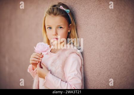 Ritratto romantico di adorabile bambina con capelli biondi e occhi blu, con abiti rosa e fiori di rosa Foto Stock