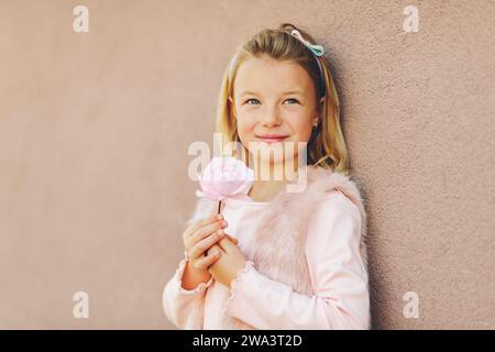 Ritratto romantico di adorabile bambina con capelli biondi e occhi blu, con abiti rosa e fiori di rosa Foto Stock