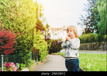 Un bambino felice che soffia il tarassino all'aperto nel parco primaverile Foto Stock