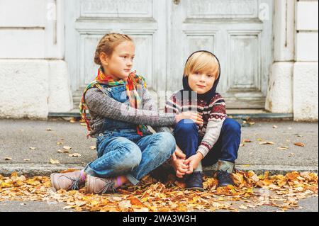 Ritratto autunnale di 2 adorabili bambini in città, con caldi pullover e jeans denim Foto Stock