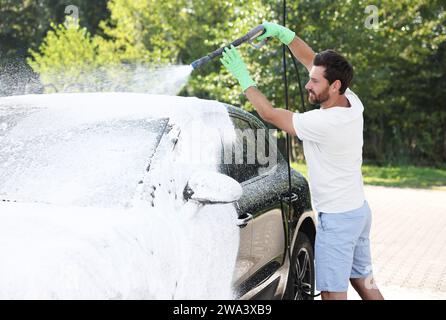 Uomo che copre l'automobile con schiuma all'autolavaggio esterno Foto Stock