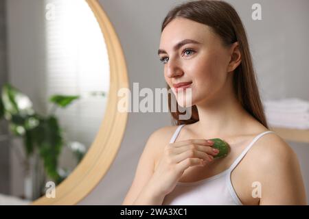 Giovane donna che applica gel di aloe dalla foglia alla spalla in bagno. Spazio per il testo Foto Stock