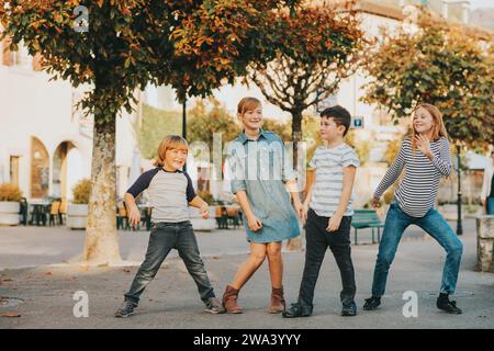 Ritratto all'aperto di 4 bambini di moda che giocano insieme all'esterno, bambini che ballano per strada Foto Stock