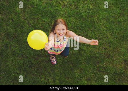 Bambina felice di 8-9 anni che gioca con la mongolfiera bianca all'aperto, vista dall'alto Foto Stock