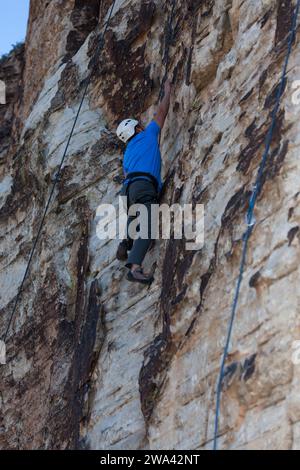 Un arrampicatore che sale per la prossima presa mentre sale dritto su una scogliera di pietra arenaria nello Utah meridionale. Foto Stock